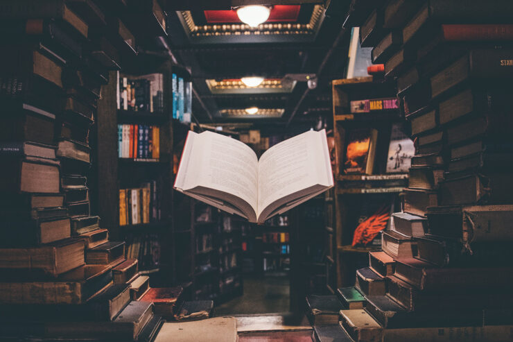 Photo of book store shelves seen through a circular frame of books; an open book is suspended in midair in the center of the photo