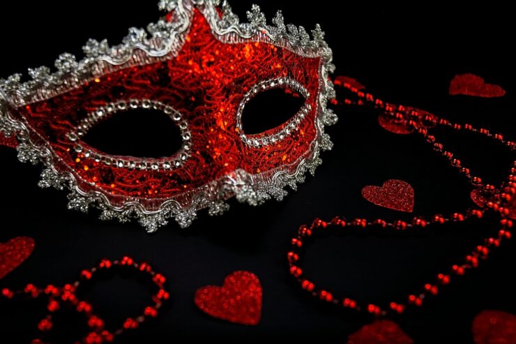 Photo of a red masquerade eye mask, red beaded necklaces, and glitter heart decorations